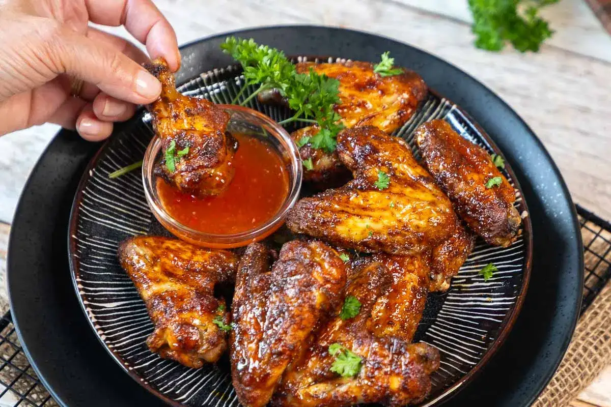 Saftige chicken wings in einer w&uuml;rzigen Marinade, die gerade in eine Schale mit Dip getaucht werden. Garniert mit Petersilie.