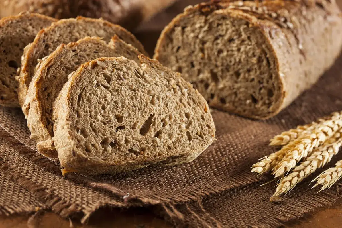 Rebanadas de pan de salvado rústico sobre tela de arpillera, con espigas de trigo al lado.