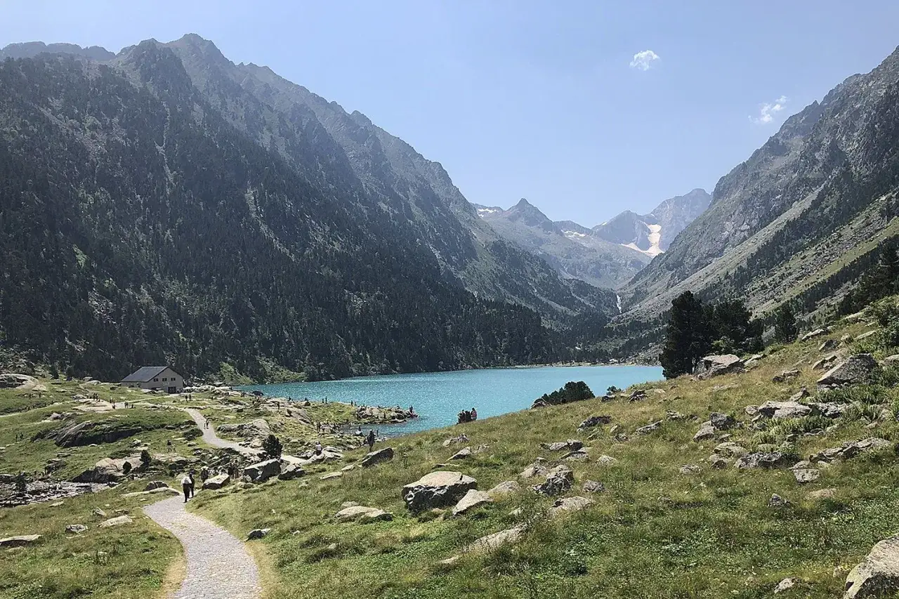 Sentier de randonnée facile dans les Pyrénées menant à un lac turquoise entouré de montagnes verdoyantes.