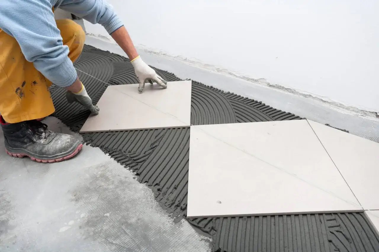 A tiler places tiles on wet adhesive. Walking on tile too soon can cause shifting and unevenness.