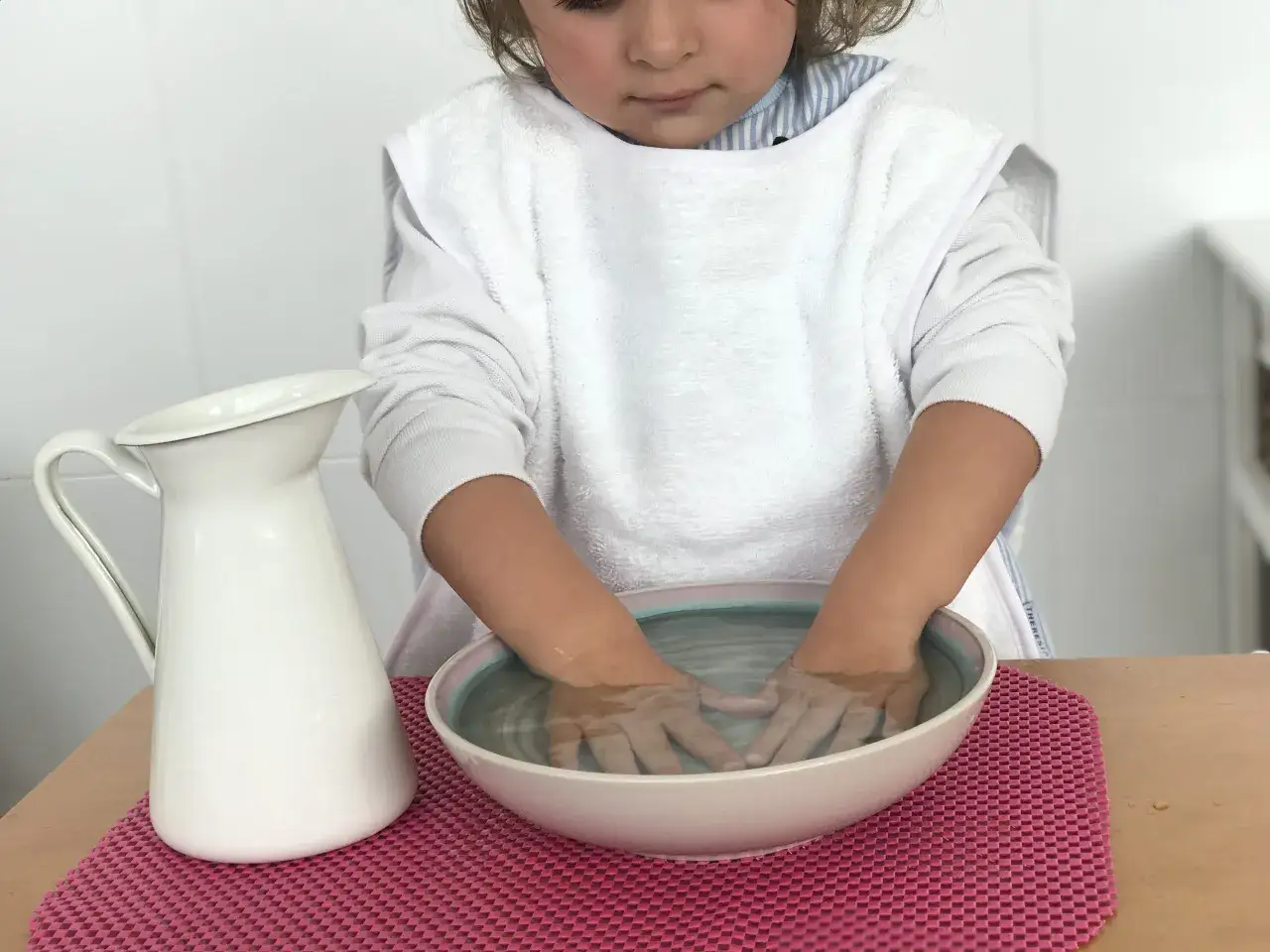 Niño concentrado realizando actividades método Montessori: lavado de manos con jarra y cuenco.