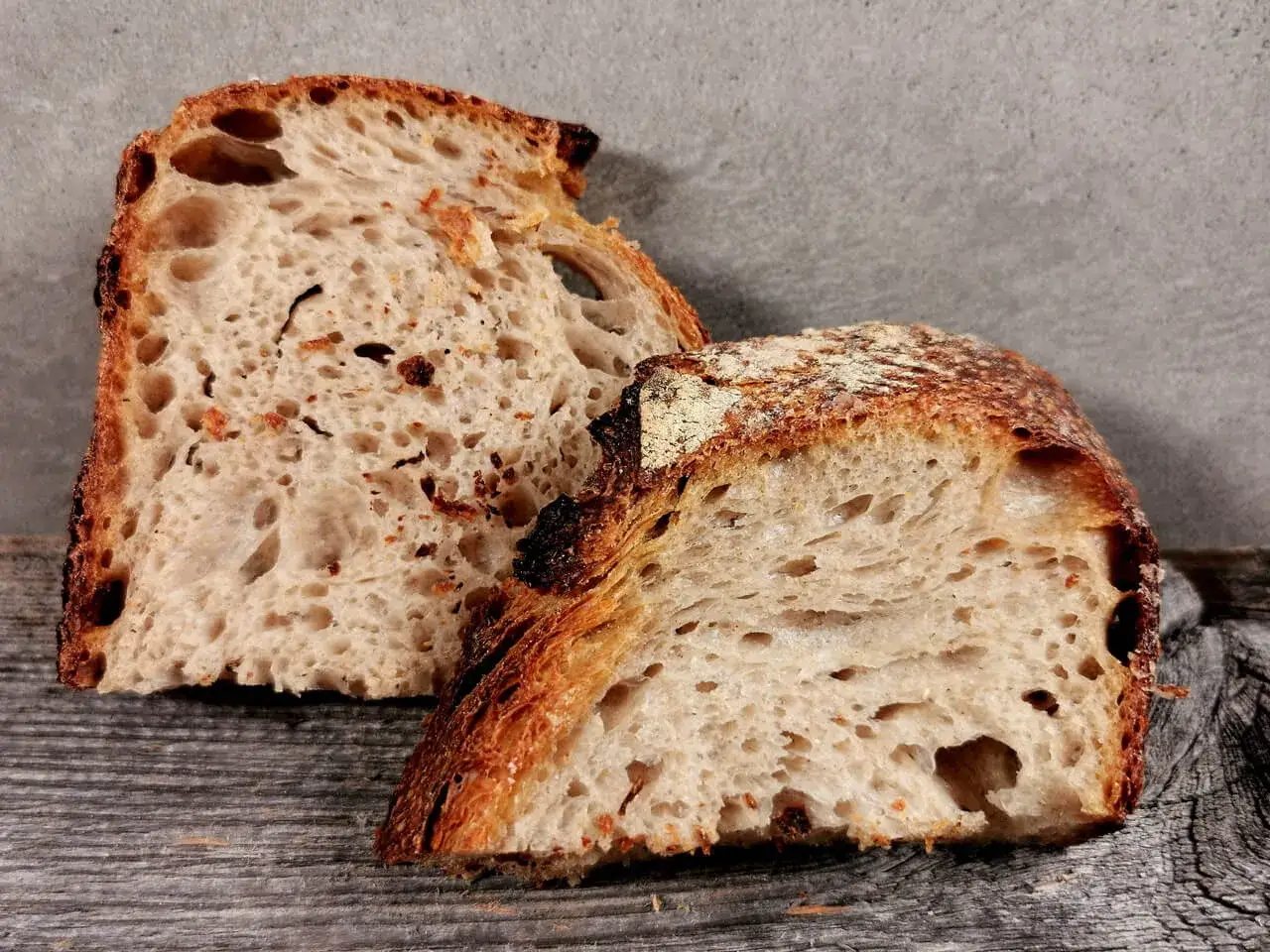 Zwei Scheiben knuspriges Sauerteig Kastenbrot mit gro&szlig;er Porung liegen auf Holz.