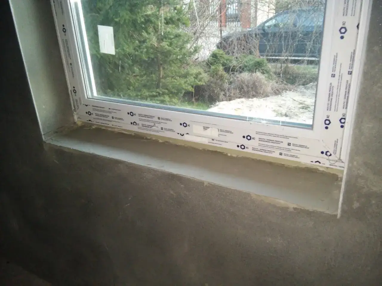 Obróbka okna w trakcie prac wykończeniowych. Widoczny parapet i fragment ściany.