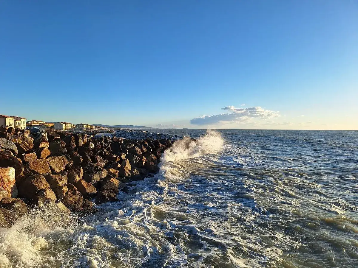 Vagues s'écrasant sur la digue de rochers à Marina di Pisa plage, sous un ciel bleu clair.
