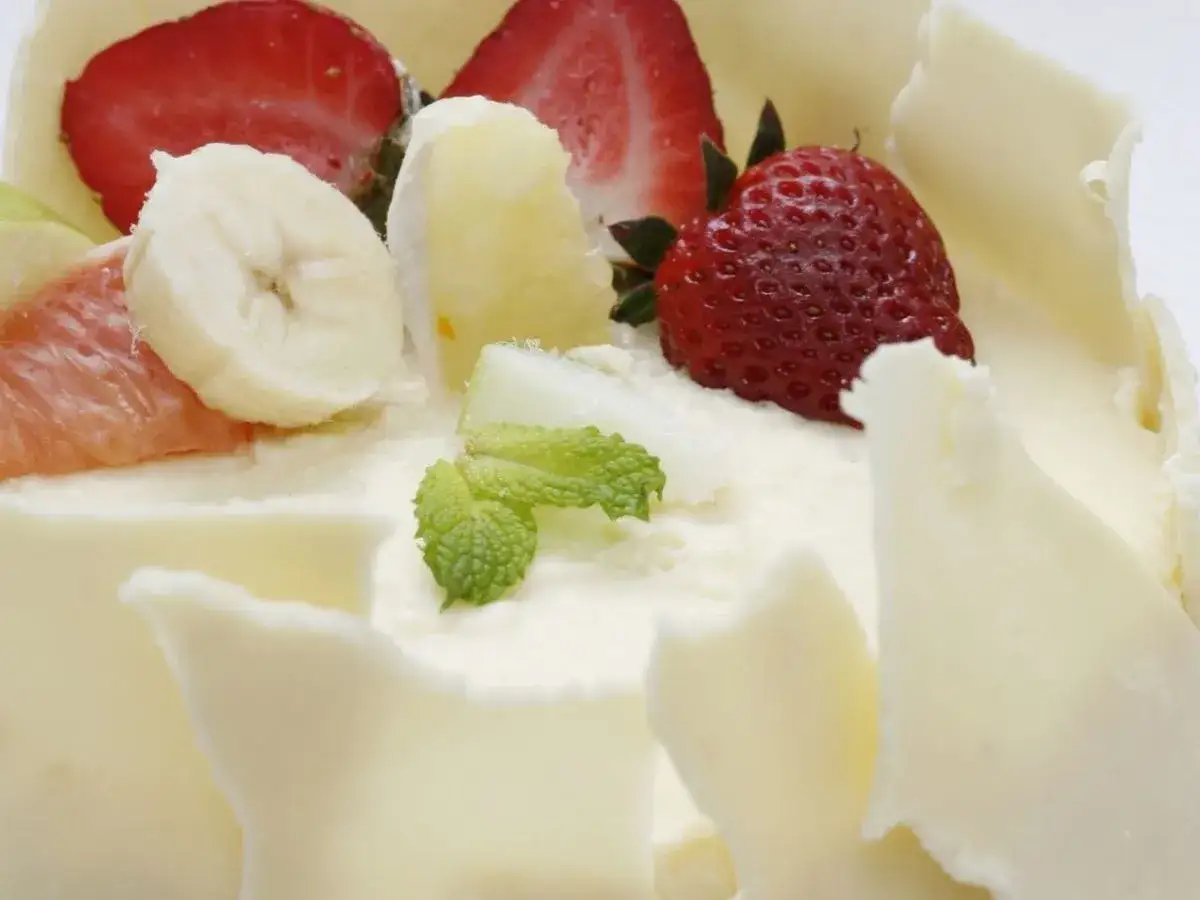 Deliciosa tarta de cuajada cubierta de chocolate blanco y decorada con fresas, plátano y menta.