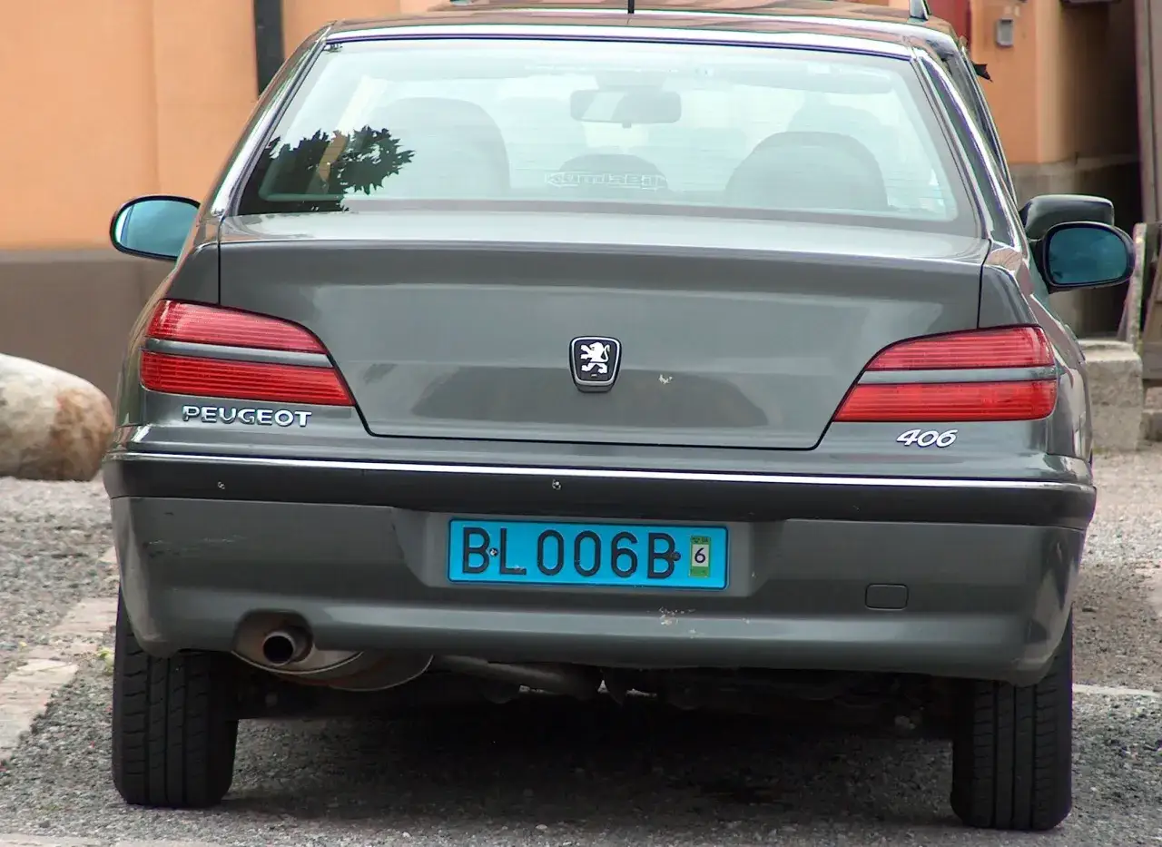 Gr&aring; Peugeot 406 med en bl&aring; registreringsskylt BL006B.