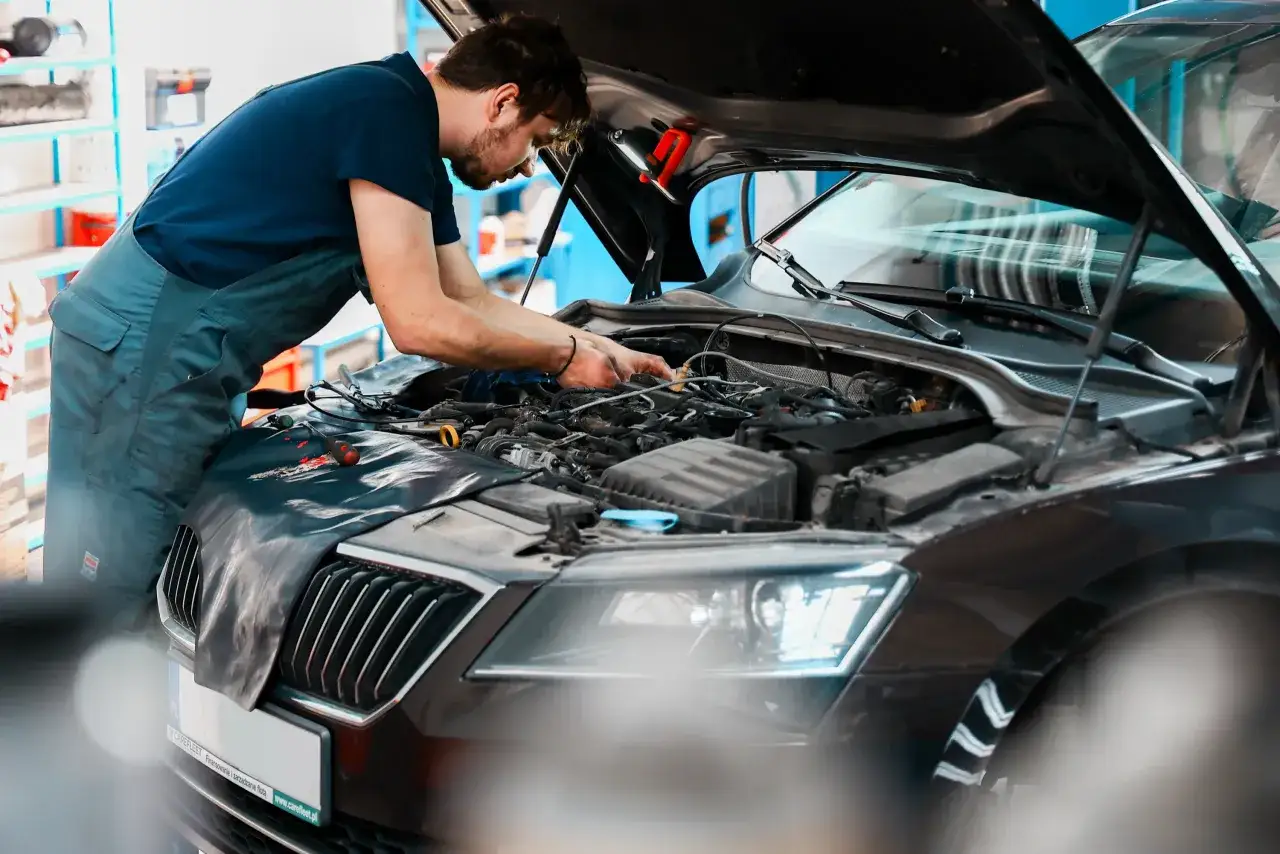 Mechanik pracuje przy silniku samochodu, kończąc docieranie turbiny po regeneracji.