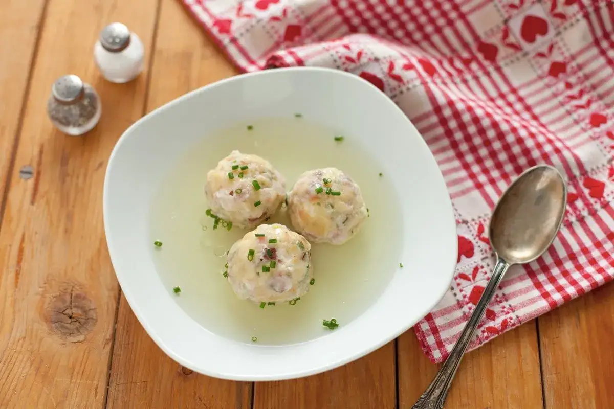 Tre canederli in brodo, guarniti con erba cipollina. Una deliziosa ricetta per un piatto confortante.