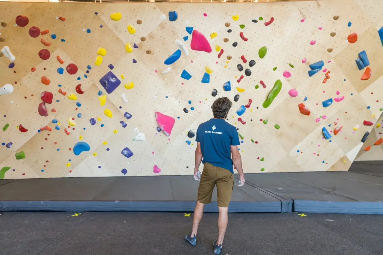 Bouldering zasady: wspinacz przygotowuje się do pokonania kolorowych chwytów na drewnianej ścianie.