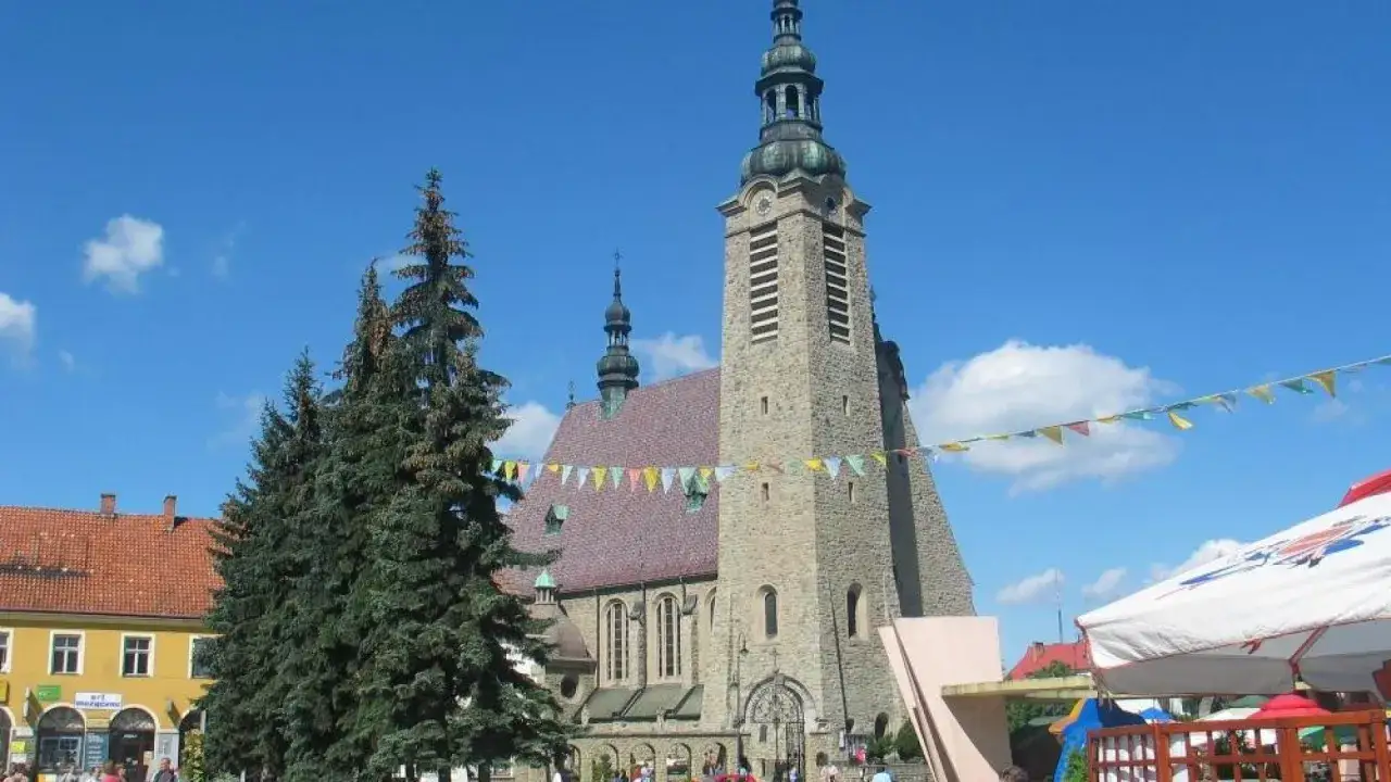 Kamienny kościół w Limanowej z wieżą i chorągiewkami na tle błękitnego nieba.