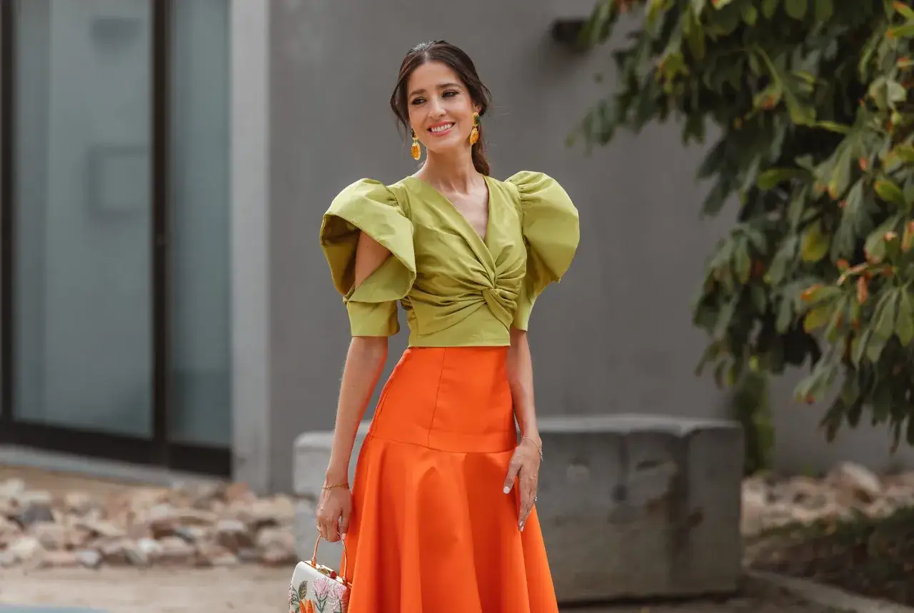 Una invitada boda oto&ntilde;o luce un top verde lima con volantes y una falda naranja vibrante.