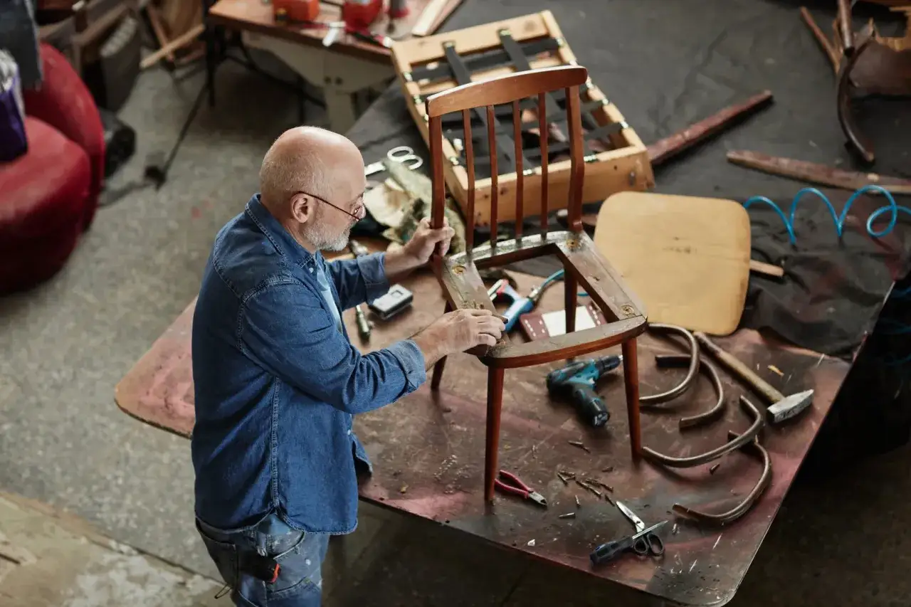 Hombre trabajando en la restauración de muebles vintage, lijando una silla de madera.
