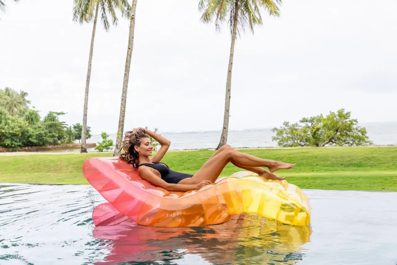 Mujer relajada en un flotador inflable de colores vibrantes, rodeada de palmeras y el mar. &iexcl;Perfecto para el vocabulario de verano!