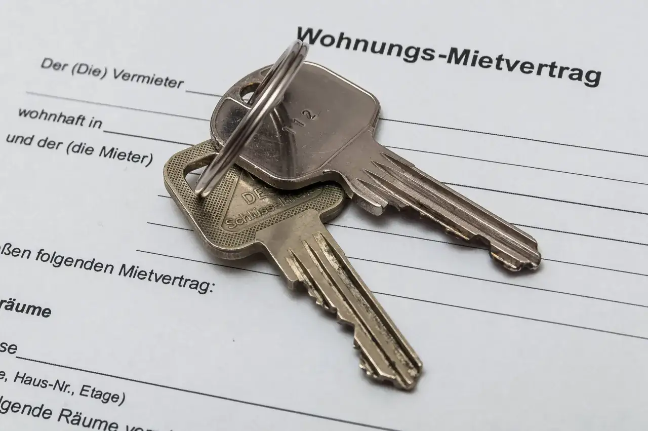 Zwei Schlüssel liegen auf einem Wohnungs-Mietvertrag. Ein kostenloser Muster Mietvertrag Haus ist hier abgebildet.
