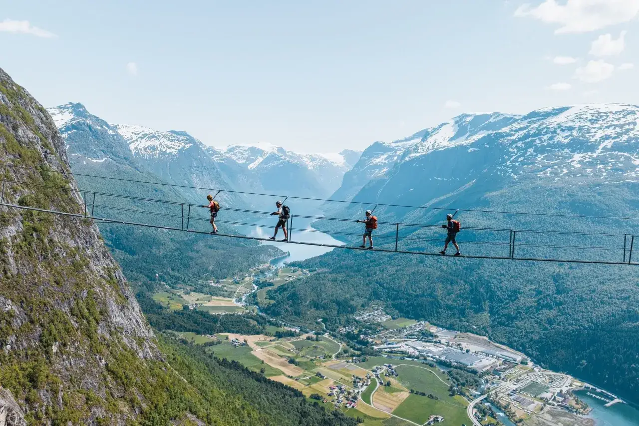 Äventyrare går på Loen via ferrata, en hängbro högt över en dal med snöklädda berg i bakgrunden.