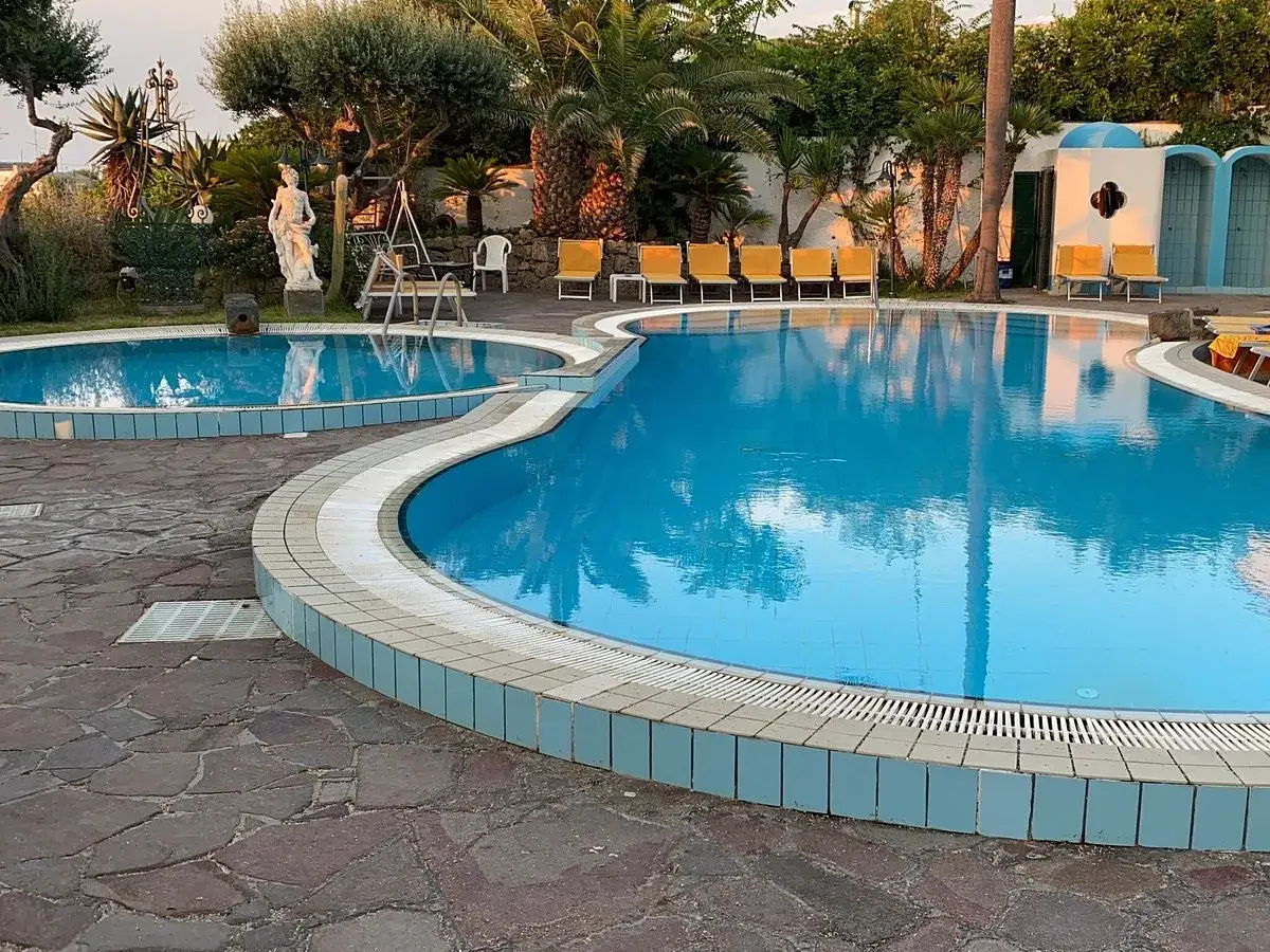 Piscine azzurre e lettini gialli al **hotel Monte Tabor**. Un'oasi di relax tra palme e statue.