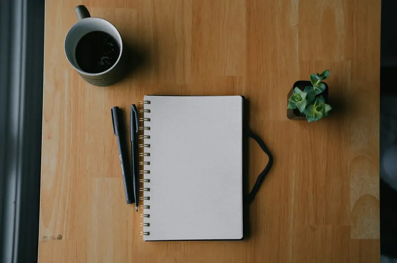 Tazza di caff&egrave;, quaderno puntinato, penne e una piccola pianta. Tutto pronto per iniziare a studiare con questi libri per imparare.