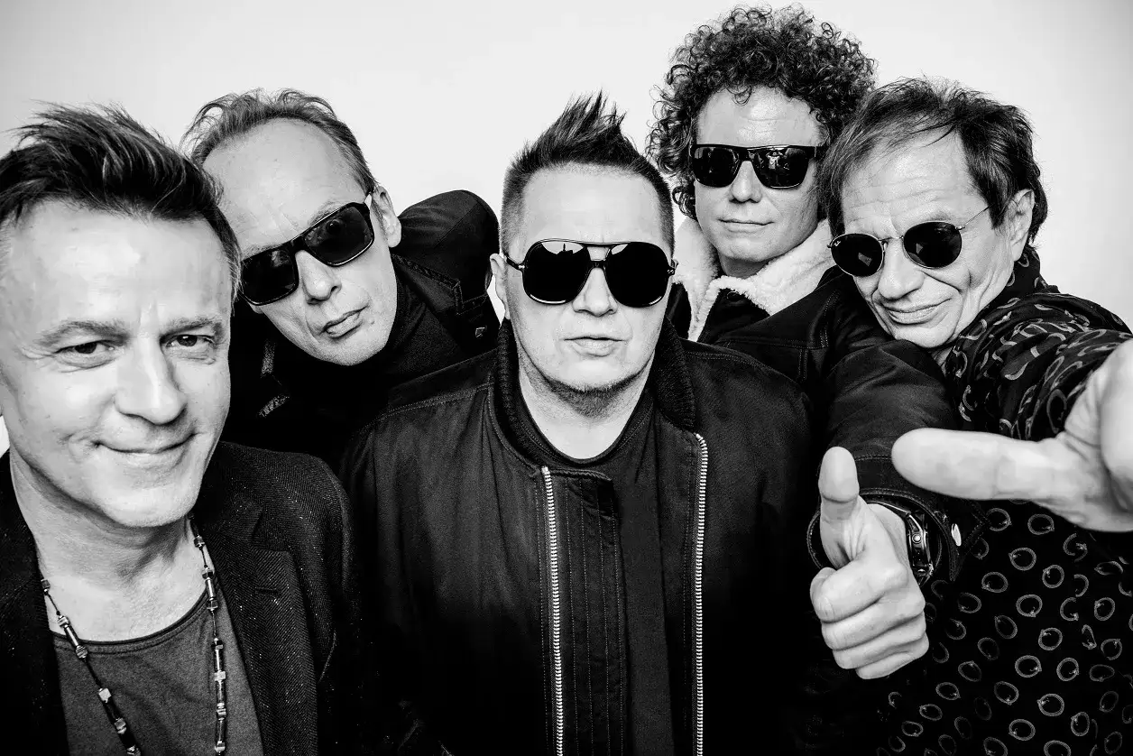 Pięciu mężczyzn w okularach przeciwsłonecznych, jakby kr&oacute;lowie rocka, pozuje do zdjęcia. Jeden z nich pokazuje kciuk w g&oacute;rę, wyrażając king t love.