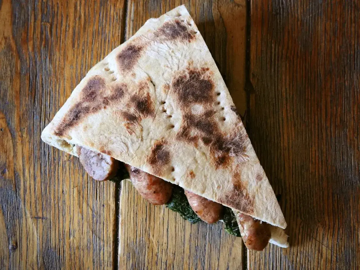 Torta al testo ripiena di salsicce e verdure, su un tavolo di legno rustico.