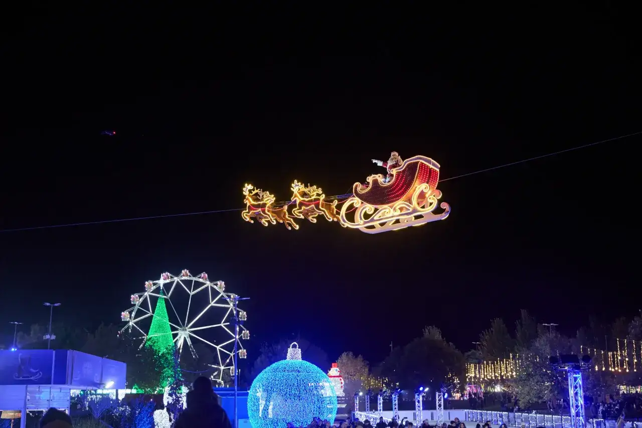 Trineo de Papá Noel ilumina la noche en la ciudad de la Navidad Madrid. Rueda de la fortuna y árbol gigante de luces brillan.