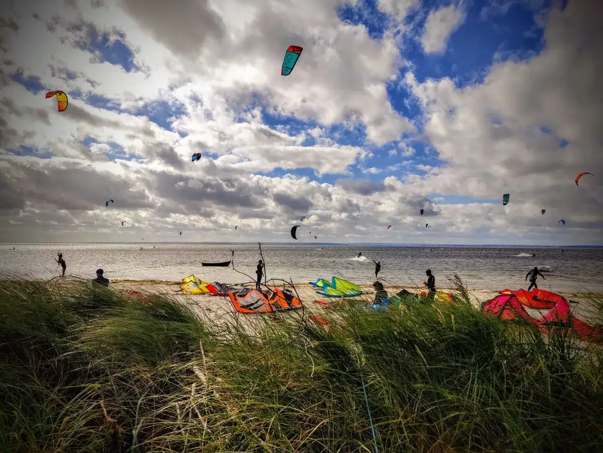 Wietrzny dzień na plaży w Kuźnicy nad morzem. Liczne kolorowe latawce kitesurfingowe unoszą się na niebie, a sportowcy szykują się do wodnych szaleństw.