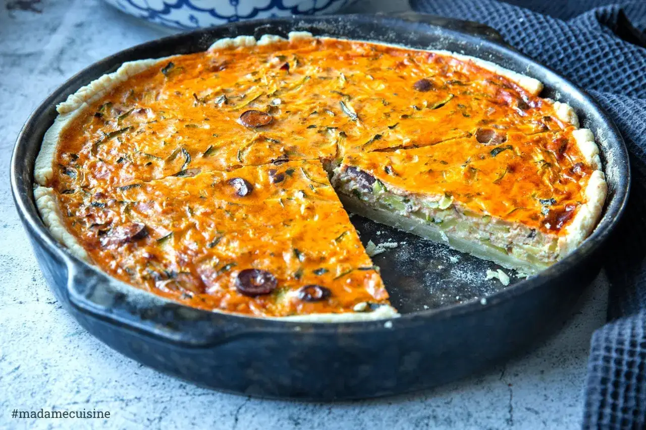 Eine herzhafte Quiche mit Zucchini und Oliven in einer Gusseisenpfanne, eine Scheibe herausgeschnitten.