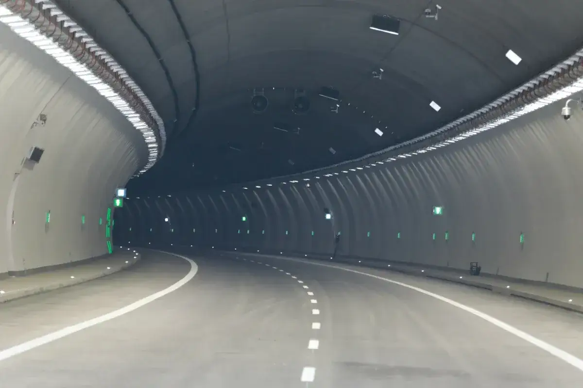 Wnętrze nowoczesnego tunelu na Zakopiance, z oświetleniem i zielonymi światłami ewakuacyjnymi.