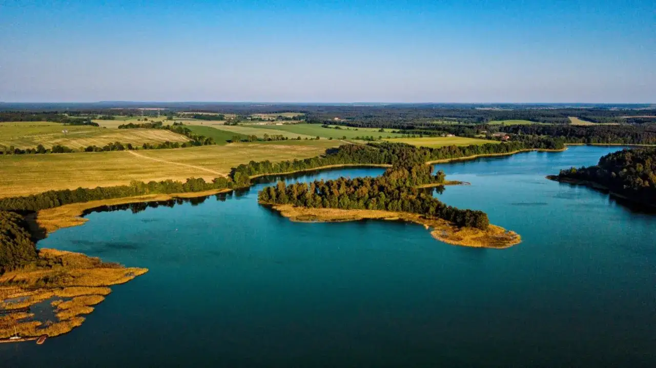 Malownicze jezioro z wyspą porośniętą drzewami, otoczone polami i lasami. Idealne miejsce na odkrywanie pojezierze wielkopolskie atrakcje.