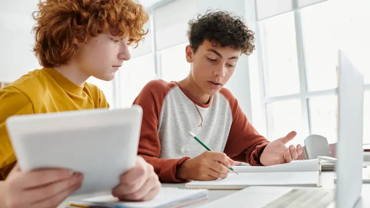Zwei Jungen lernen gemeinsam. Einer h&auml;lt ein Tablet, der andere schreibt in ein Notizbuch. Moderne **apps studium** helfen ihnen dabei.