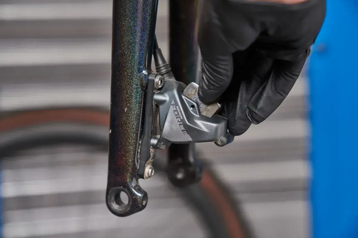 En hand med svart handske tar bort en bromskloss fr&aring;n en cykelbroms. Dags att byta bromsklossar p&aring; cykeln f&ouml;r b&auml;ttre bromskraft.