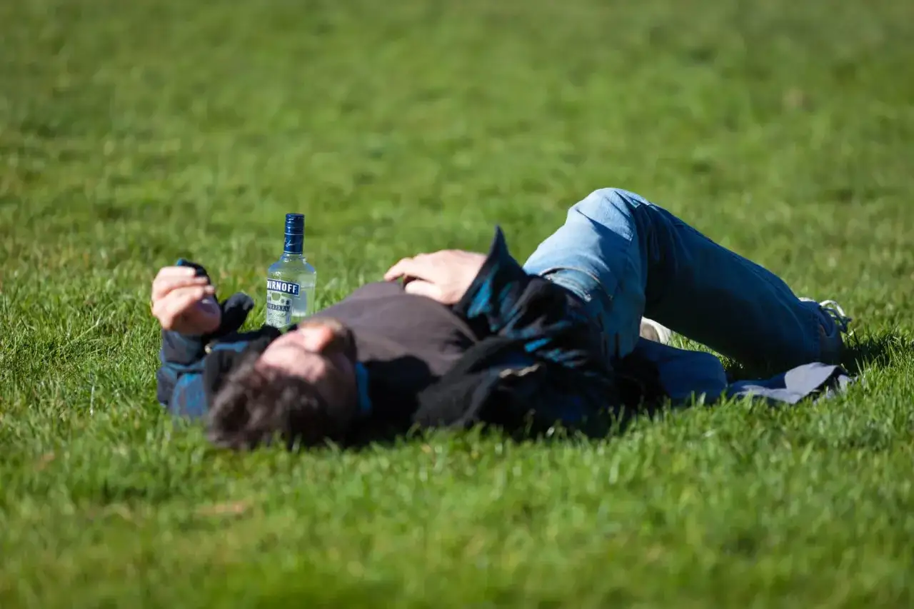 Mężczyzna leży na trawie obok butelki alkoholu. Może to być obraz przedstawiający skutki nadużywania substancji, takie jak padaczka po narkotykach.