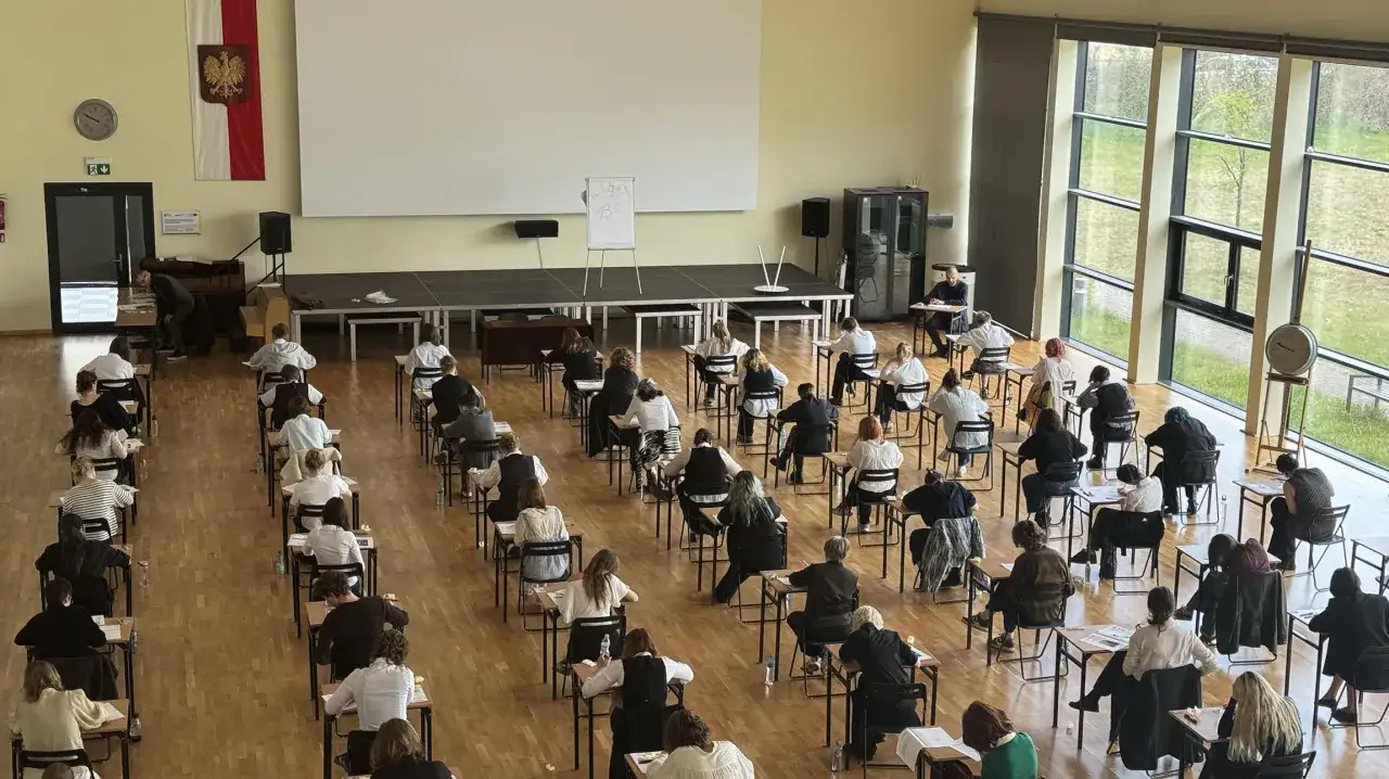 Uczniowie piszą **matura szkoła w chmurze** – sala gimnastyczna zamieniona na salę egzaminacyjną, z rzędami ławek i skupionymi twarzami.
