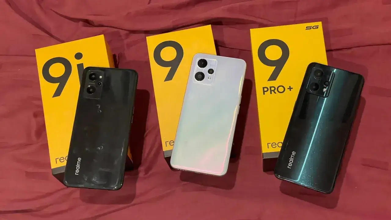 Trzy telefony realme 9a w różnych kolorach: czarnym, białym i zielonym, obok żółtych pudełek z logo