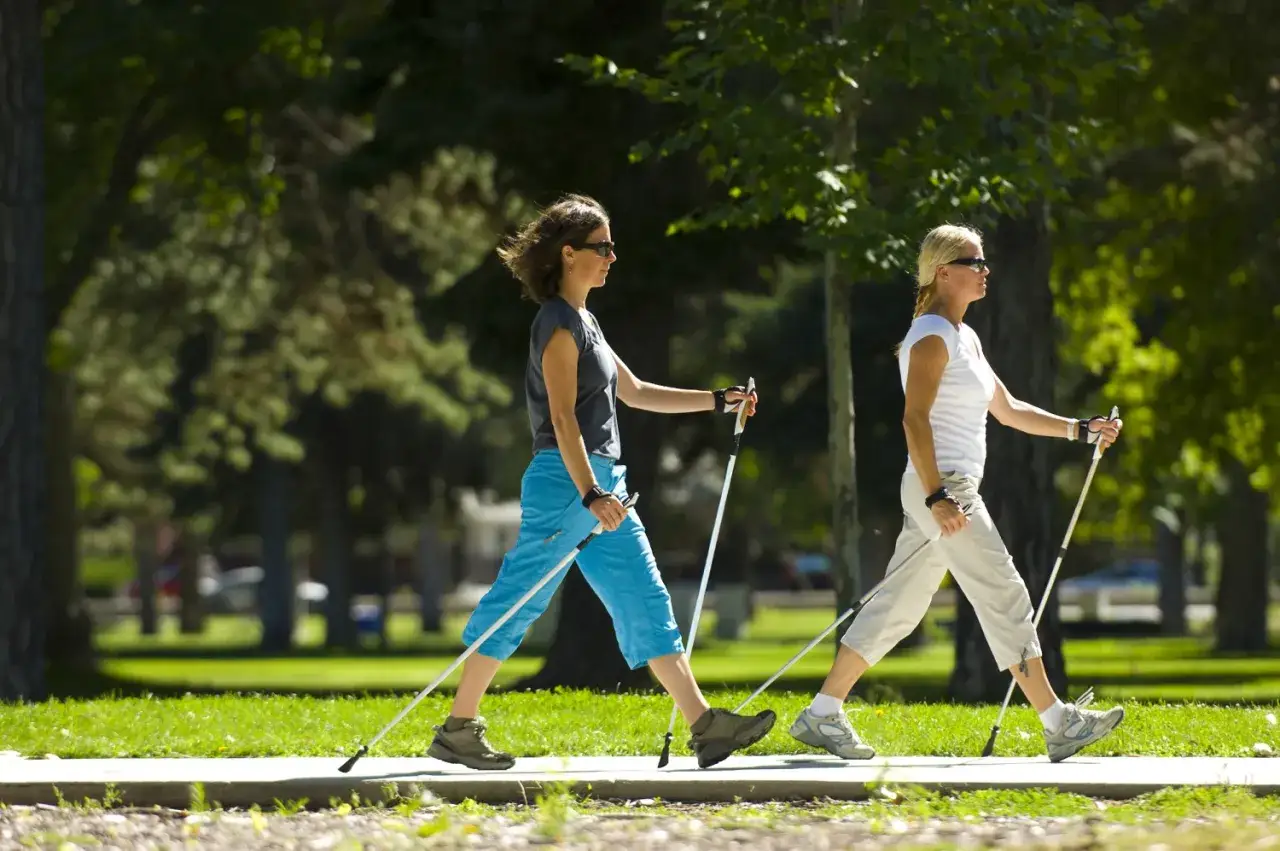 Dwie kobiety uprawiające nordic walking w parku. Dowiedz się, jak dobrać kije do nordic walking, by spacer był efektywny i przyjemny.