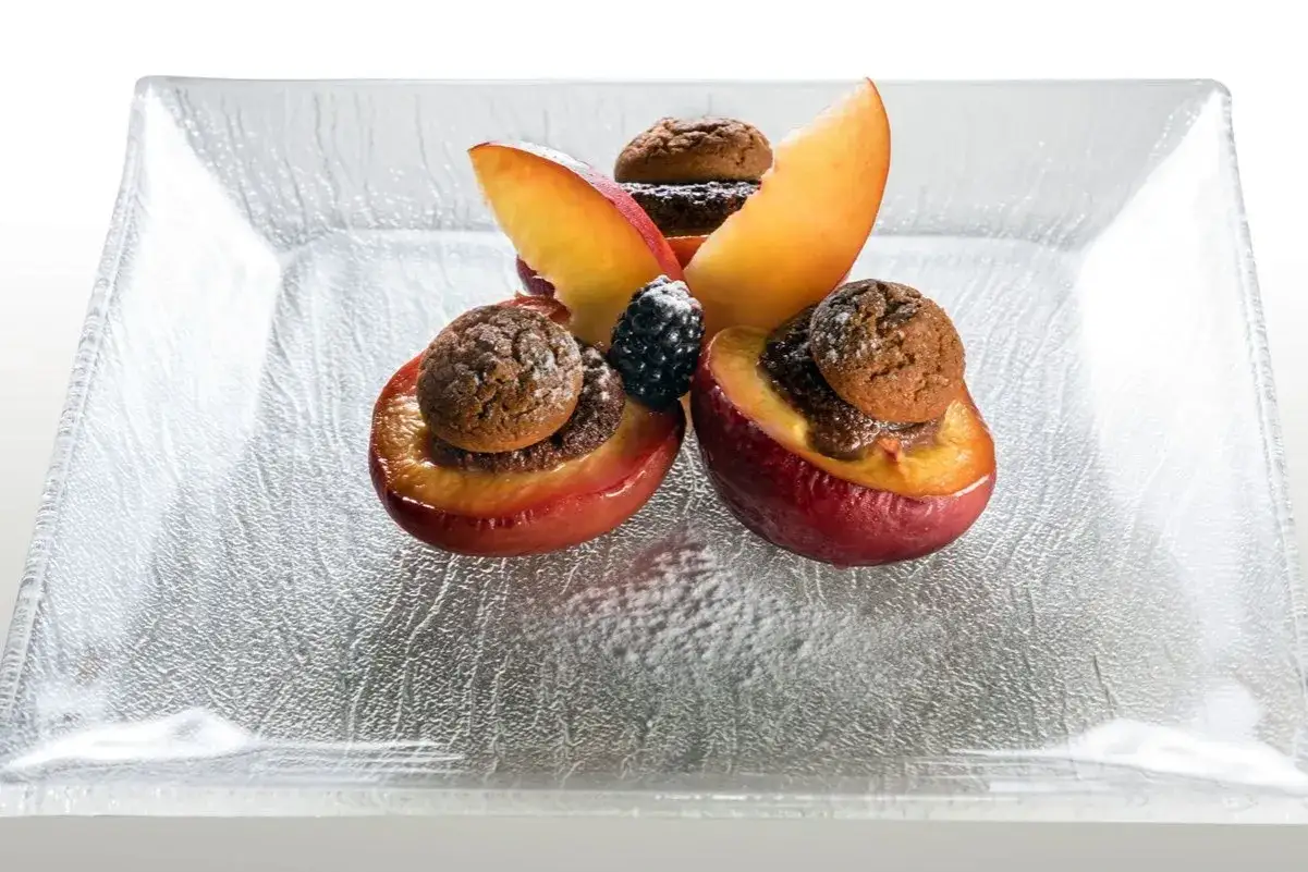 Deliziose pesche ripiene con biscotti e frutti di bosco, un dolce invitante su un piatto di vetro.