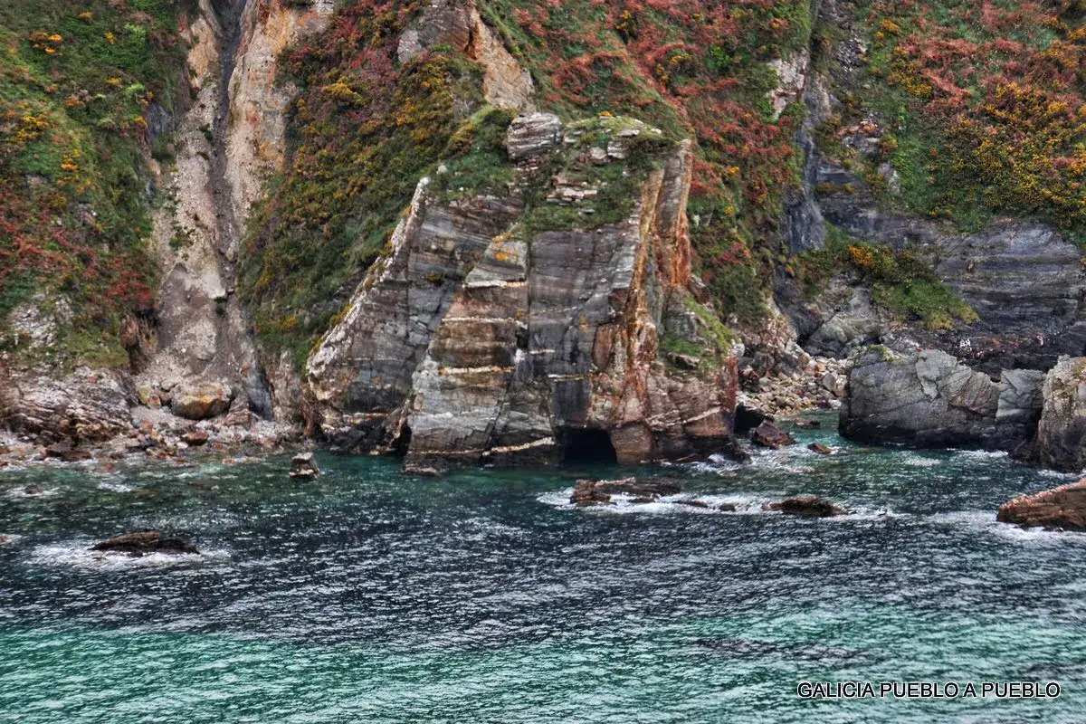 Acantilados verdes y rocosos con cuevas marinas, aguas turquesas y el mar agitado. Un paisaje natural para descubrir qué ver en O Vicedo.