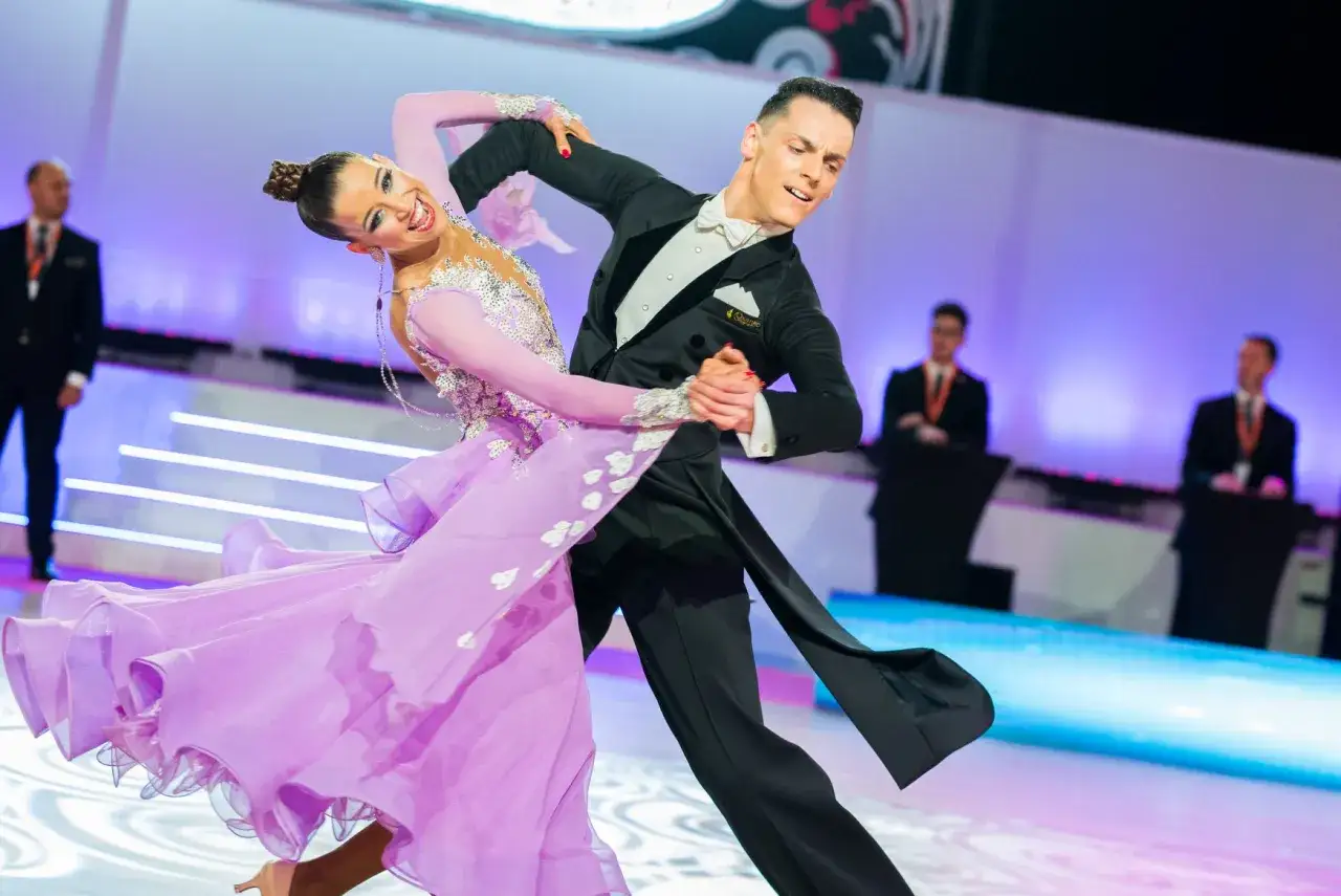 Pareja de baile de salón en competición, ella con vestido lila, él con frac. Demuestran que el baile es un deporte.