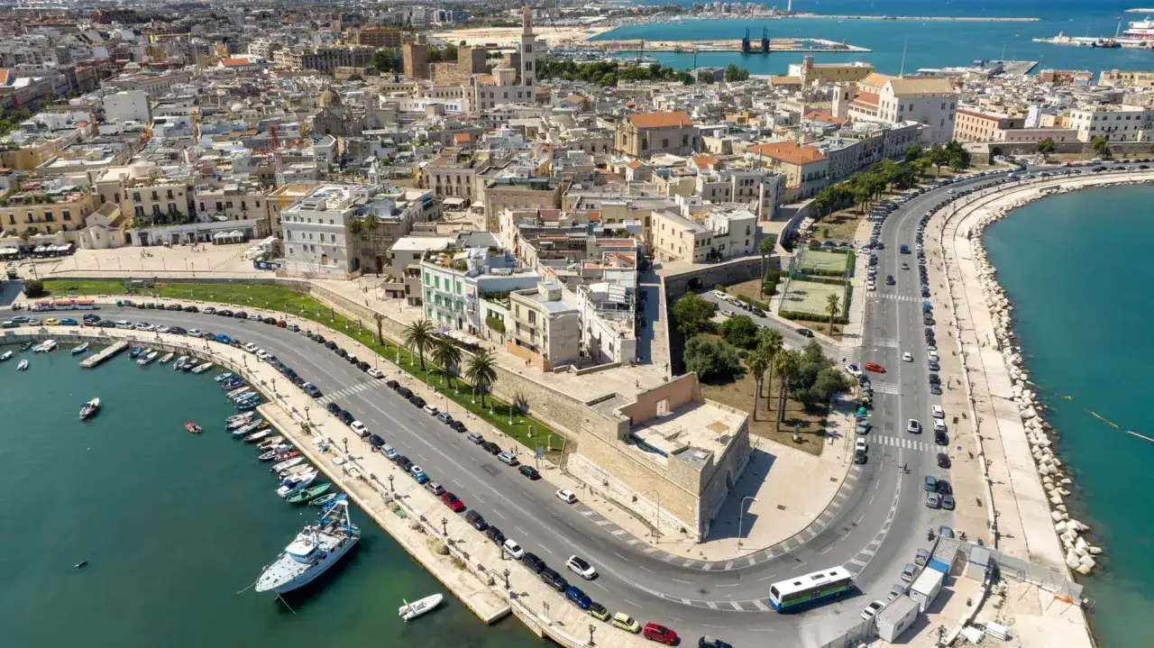 Vista aerea del lungomare di Bari, il capoluogo della Puglia, con barche ormeggiate e la città che si estende verso il mare.