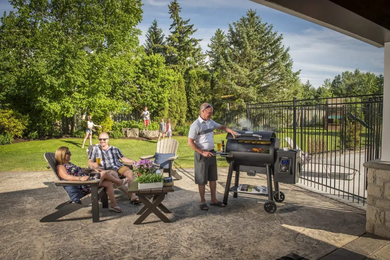 Rodzina cieszy się latem przy grillu z wędzarnią. Dzieci bawią się na trawniku, a dorośli relaksują się przy napojach.