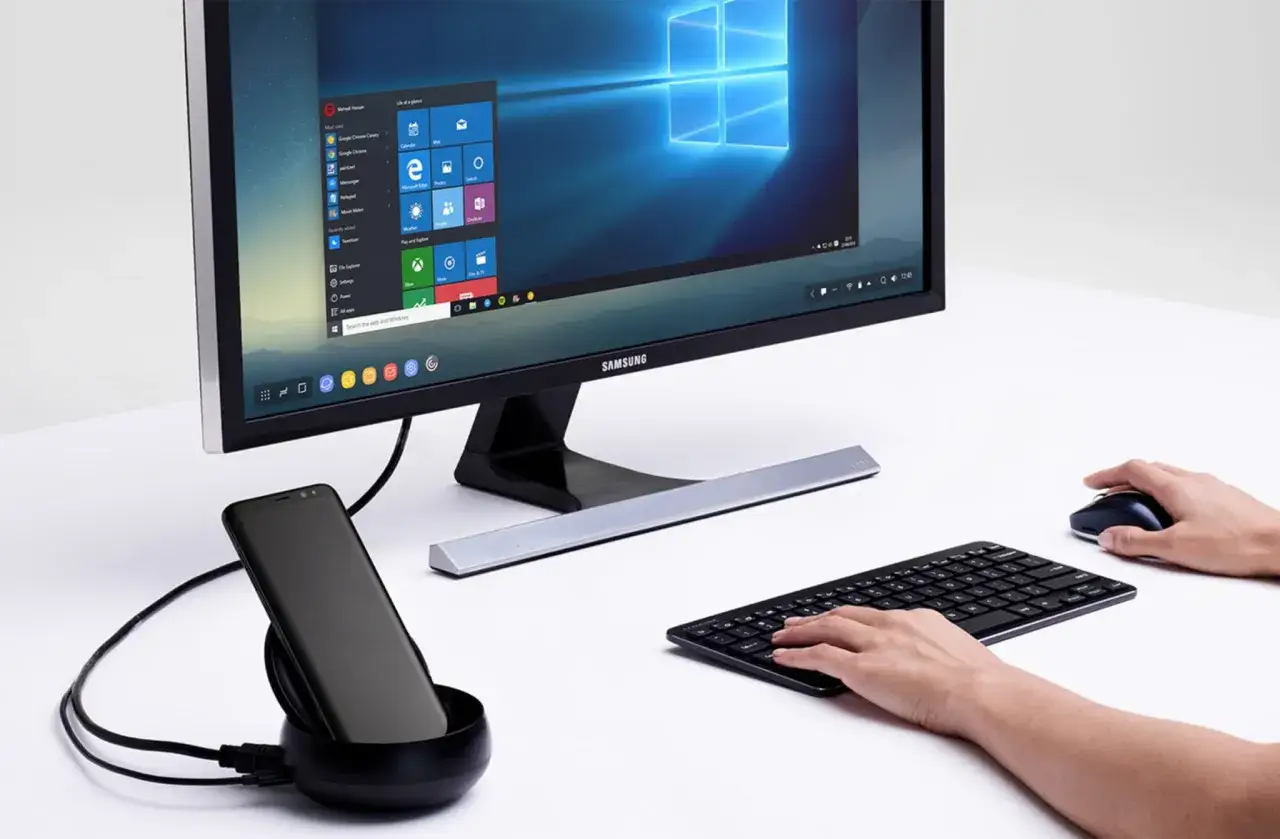 Samsung DeX zamienia smartfon w komputer. Na monitorze widoczny jest pulpit Windows, a obok klawiatura i myszka.