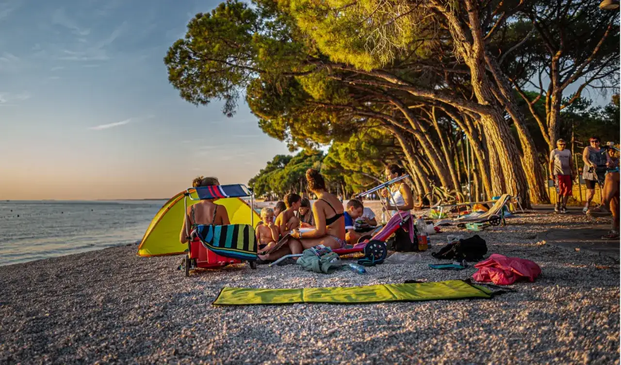 Rodzina cieszy się słońcem i morzem podczas rodzinnego **camping oliva**. Dzieci bawią się pod parasolem, a dorośli odpoczywają na plaży.