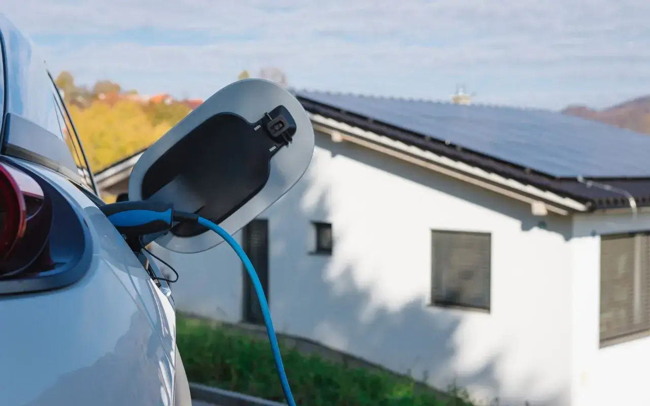 Cargando coche el&eacute;ctrico en casa con placas solares. Energ&iacute;a limpia para un futuro sostenible.