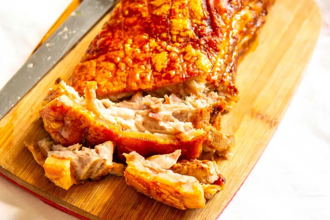 Poitrine de porc croustillante, coup&eacute;e en morceaux sur une planche en bois. La peau dor&eacute;e et craquante contraste avec la chair tendre.
