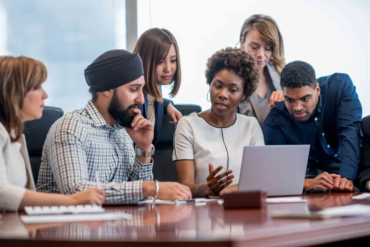 A diverse team collaborates around a laptop, showcasing inclusive business practices.