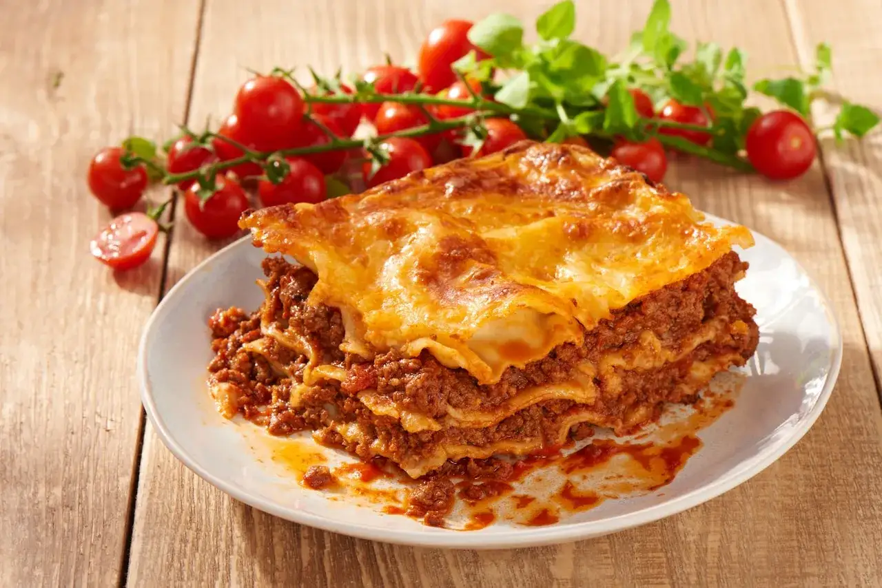 Pyszna, wielowarstwowa lasagne z mięsem mielonym i sosem pomidorowym, podana z gałązką pomidorków koktajlowych. Idealna na obiad.