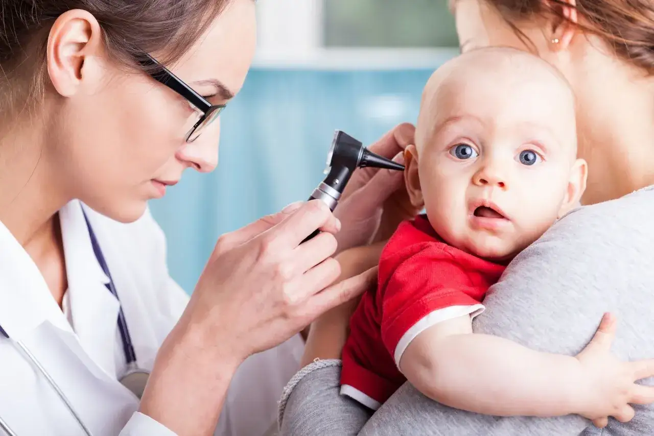 dziecko z bólem ucha, mama pociesza dziecko, objawy bólu ucha u niemowlaka