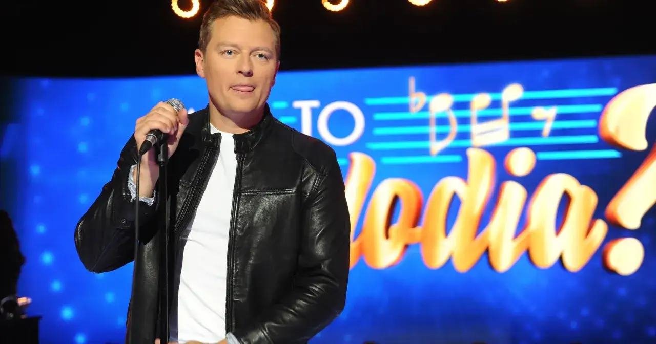 Rafał Brzozowski z mikrofonem na scenie, w tle napis