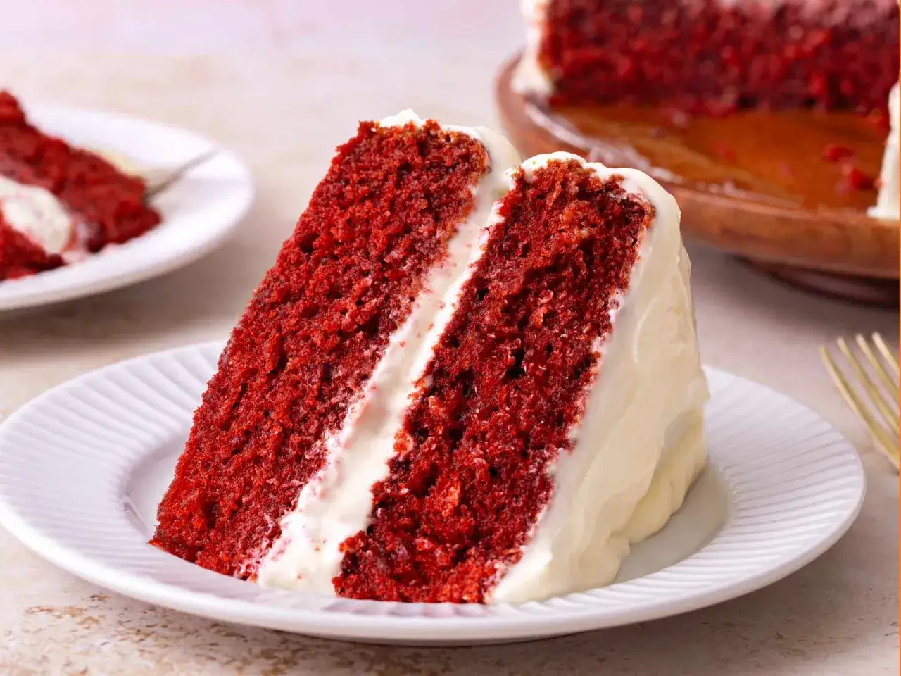 En saftig bit red velvet cake med krämig frosting. En annan bit syns i bakgrunden.