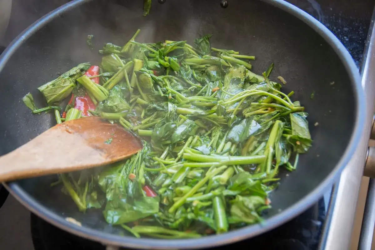 Cicoria in padella, con peperoncino e un mestolo di legno che mescola le verdure fumanti.