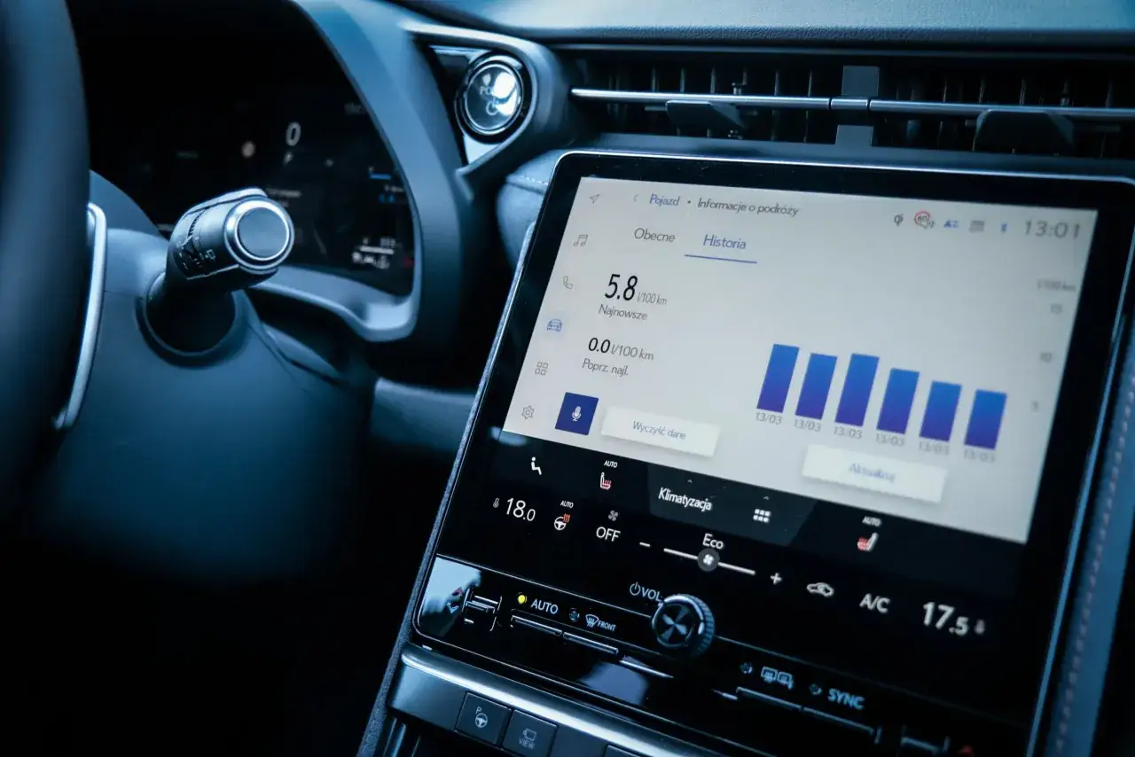 Wnętrze samochodu z ekranem multimedialnym pokazującym historię spalania, z ikoną Yanosik w tle. Android Auto działa płynnie.
